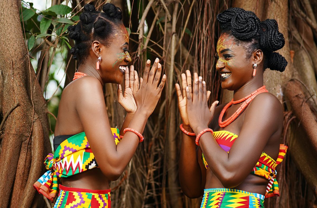 A picture containing Two African Women from Ghana Playing Together in the outdoor next to tree wearing African clothing